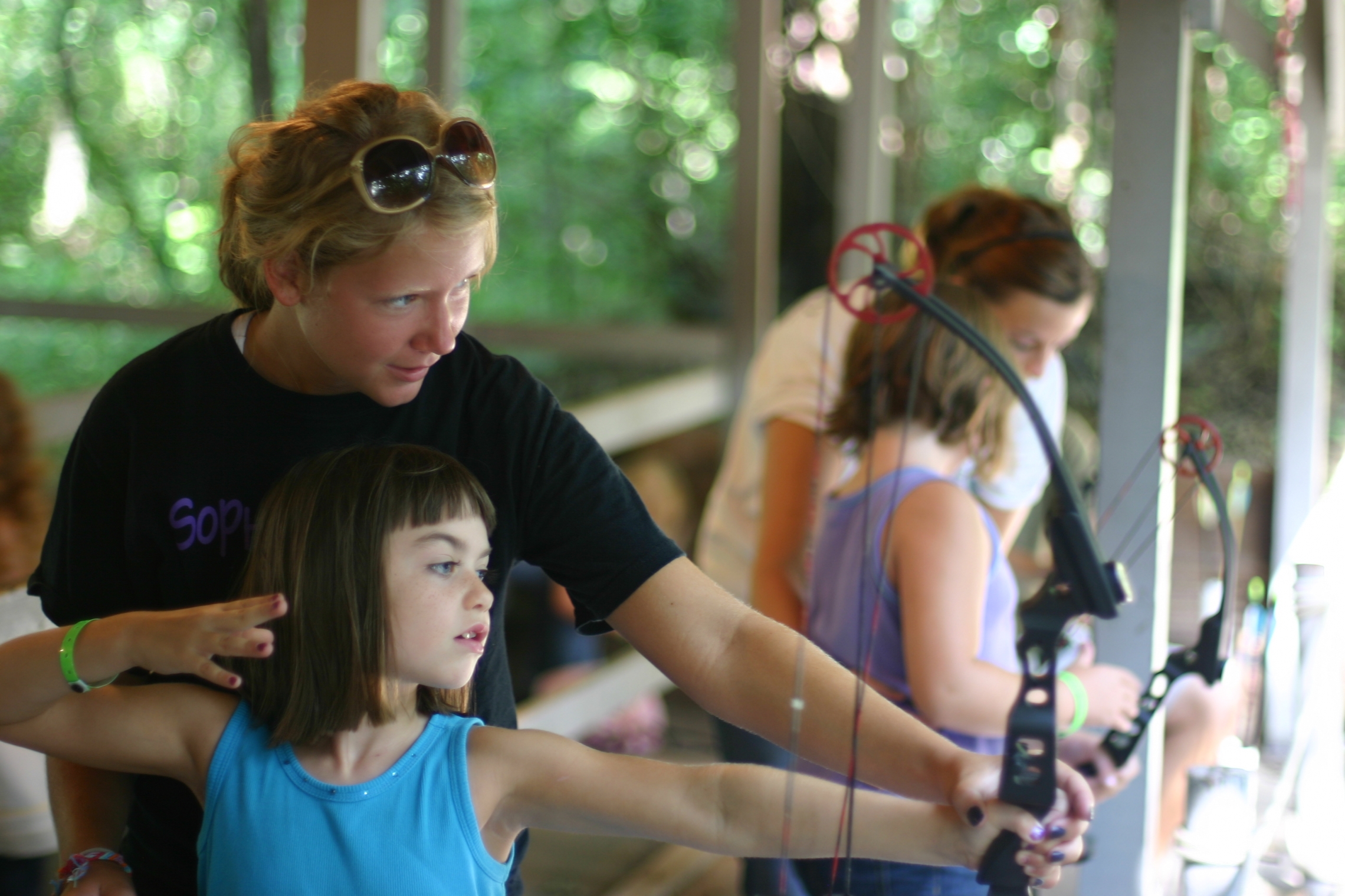 A staff member teaches a camper to shoot archery