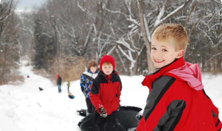 A young boy smiles over his shoulder at the top of a sled hill