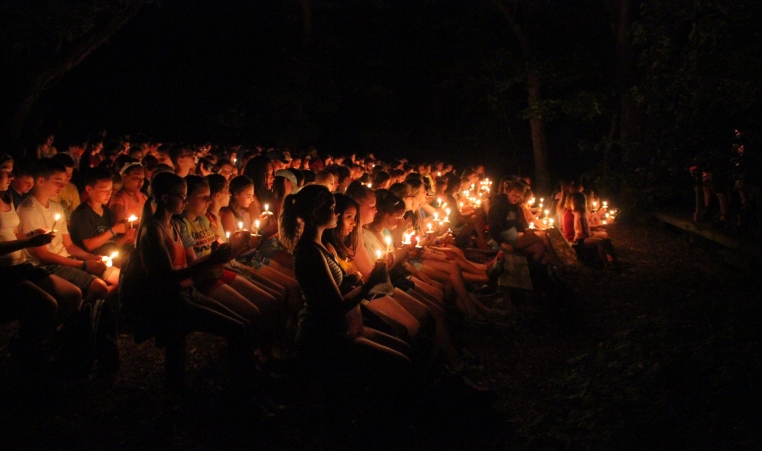 An audience sits on benches holding candles