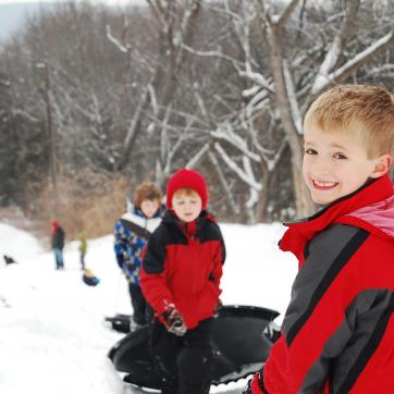 A young boy smiles over his shoulder at the top of a sled hill