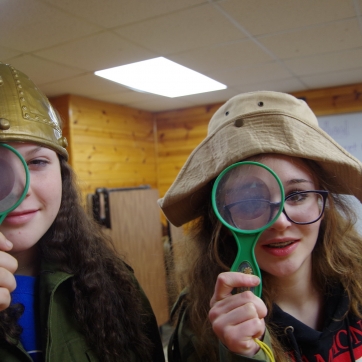 Two campers in costumes hold up magnifying glasses to their eyes.
