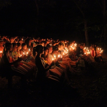 An audience sits on benches holding candles